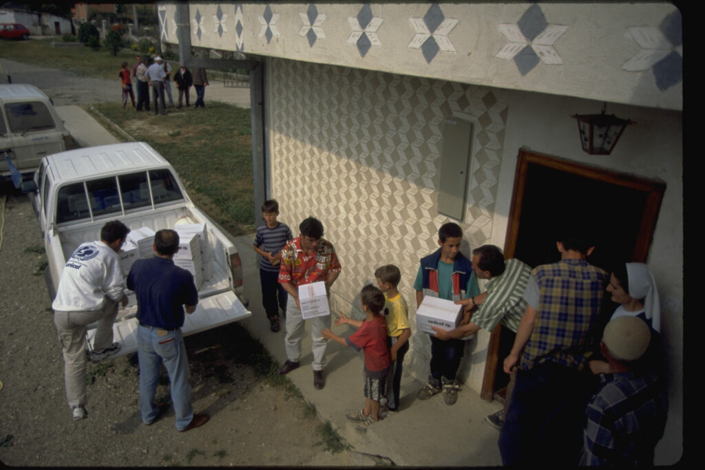 Kinderen en andere bewoners helpen UNICEF-medewerkers bij het uitladen van hulpgoederen uit een pick-uptruck en het naar binnen brengen ervan in een gebouw in het Kosovaarse dorp Glodzane. De UNICEF-medewerkers waren de eerste mensen van buiten het dorp die de bewoners zagen sinds het begin van de oorlog. Credits foto: © UNICEF/UNI31830/Horner